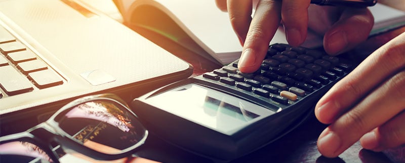 hands using calculator next to computer with sunglasses