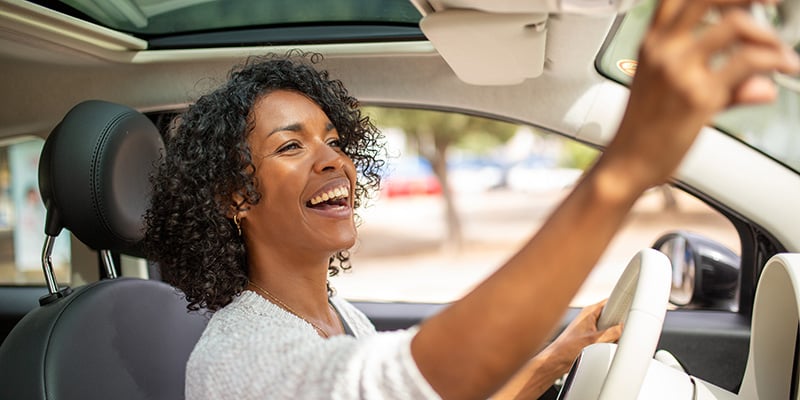 woman in new car adjusting rearview mirror